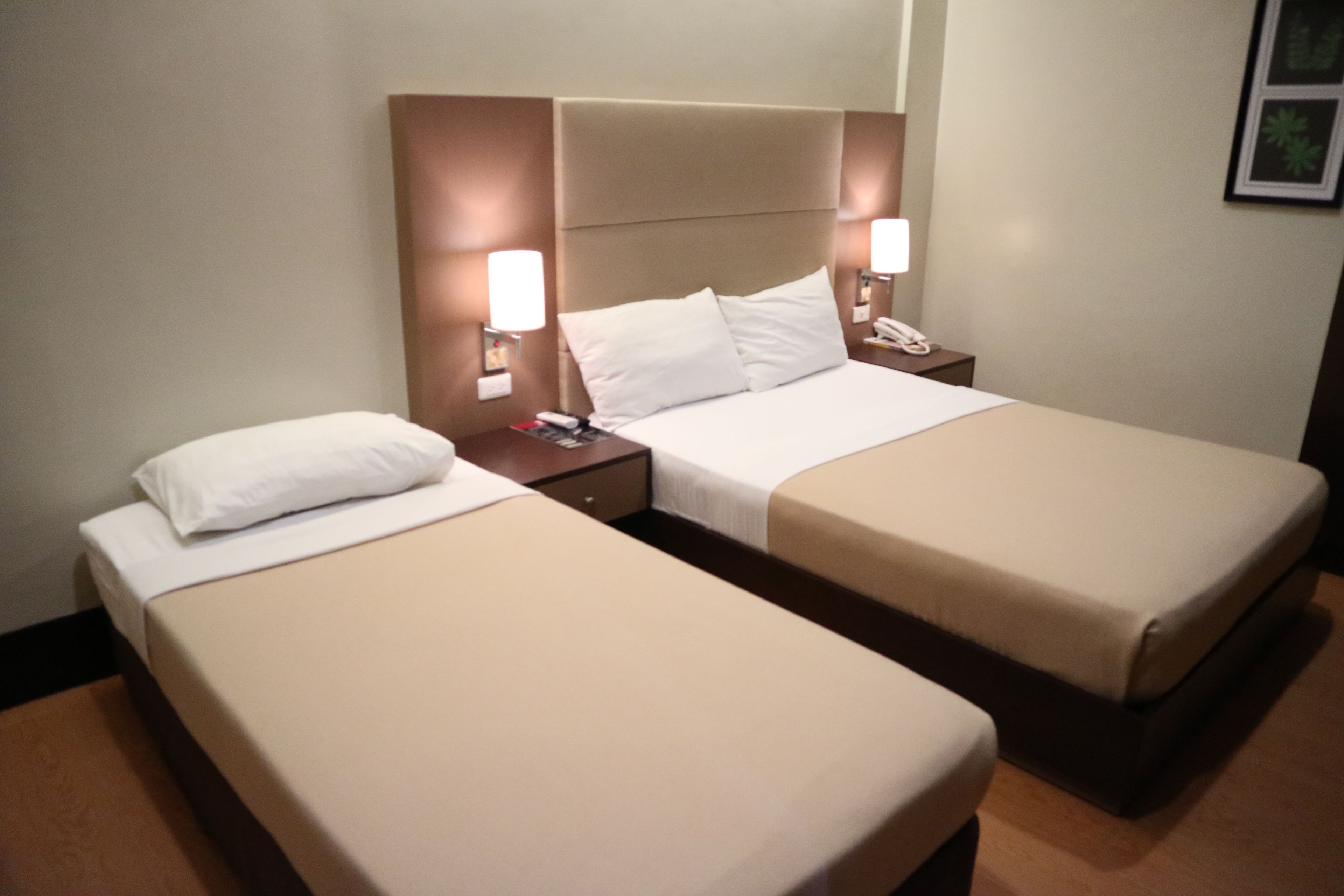 A hotel room with two single beds, each with a headboard, bedside tables, and lamps.