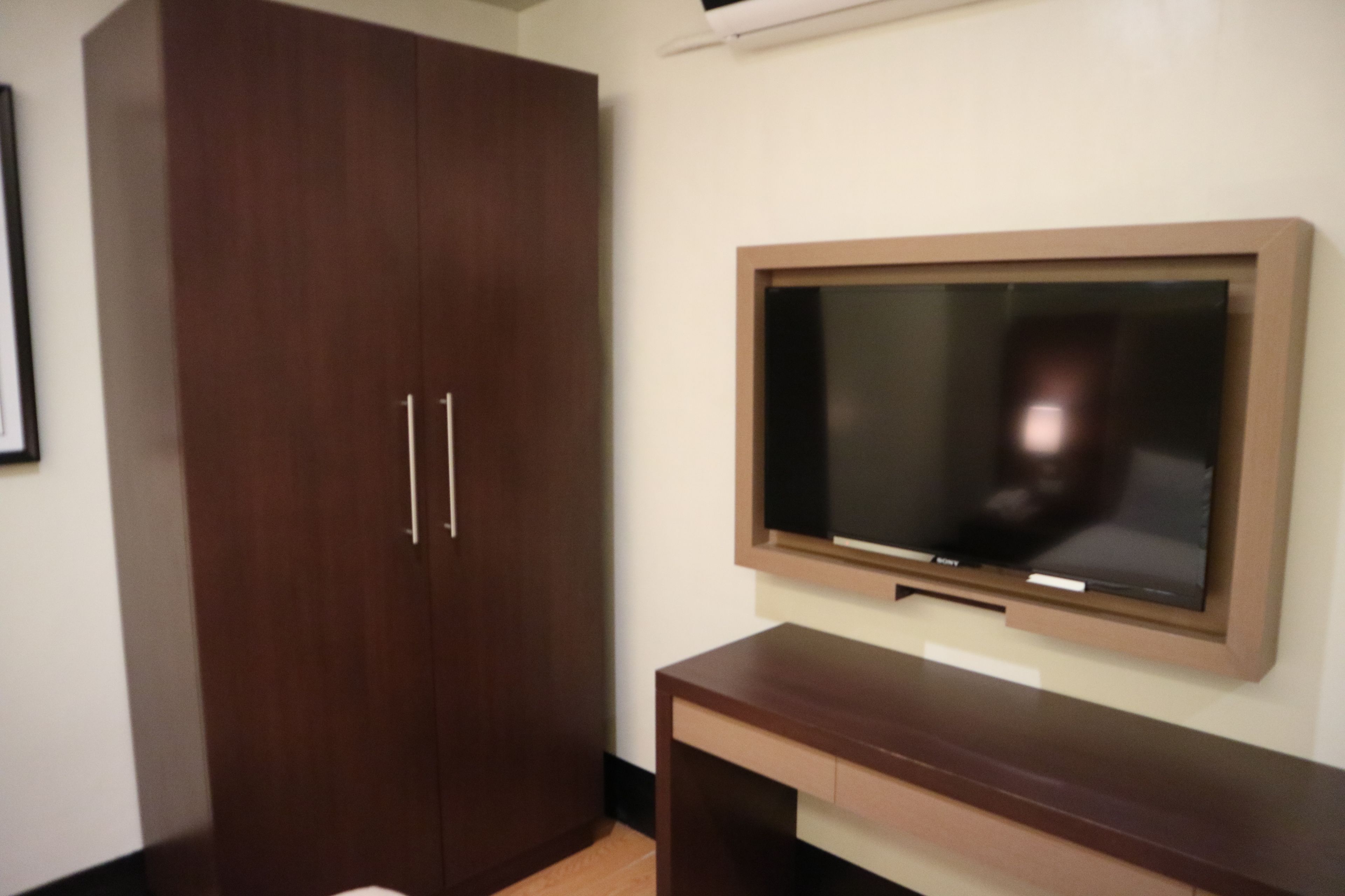 A room with a wooden wardrobe, a flat-screen TV mounted on the wall, and a wooden console table.