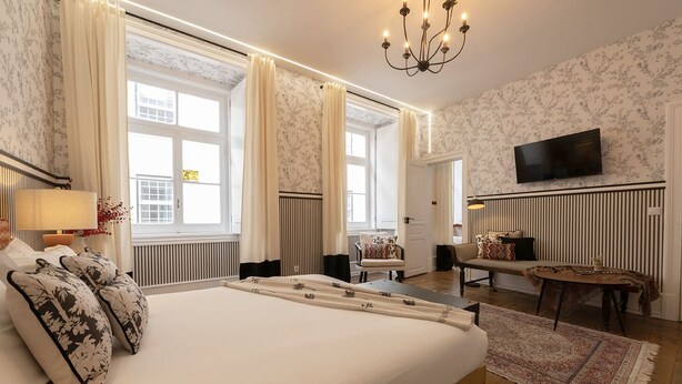 A hotel room with a large bed, a TV mounted on the wall, and a view of the city through the windows.