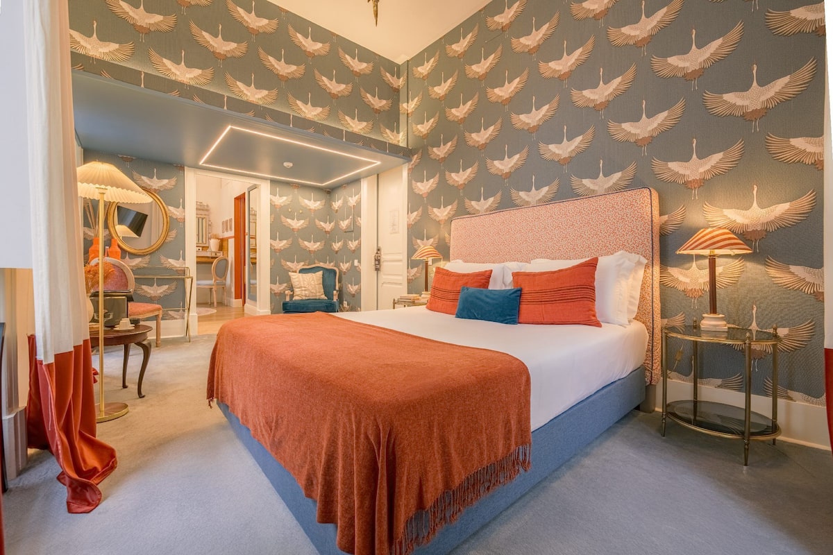 A bedroom with a large bed, a nightstand, a mirror, and a chair.