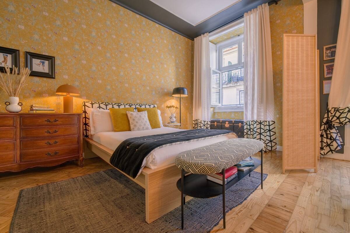 A bedroom with a bed, bedside tables, a dresser, and a window with curtains.