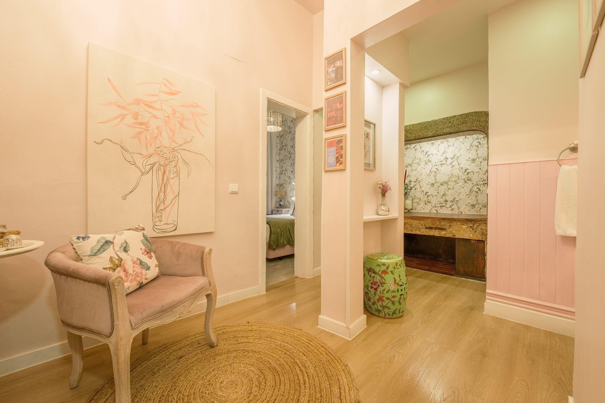 A cozy room with a wooden floor, a floral-patterned sofa, a green ottoman, and a painting of a vase with flowers.