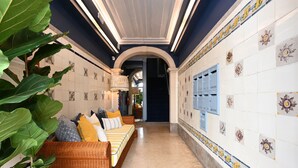 A hallway with a sofa, large plant, and tiled walls with floral patterns.