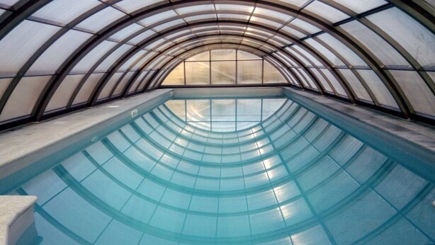 Una amplia piscina interior con techo de cristal curvo.