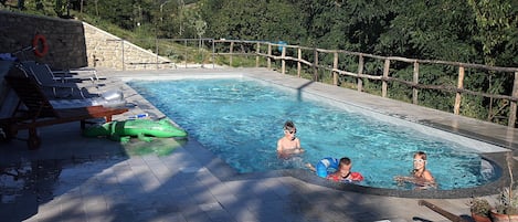 Ein Swimmingpool mit Steinmauer, Liegestühlen und einer Holzterrasse.
