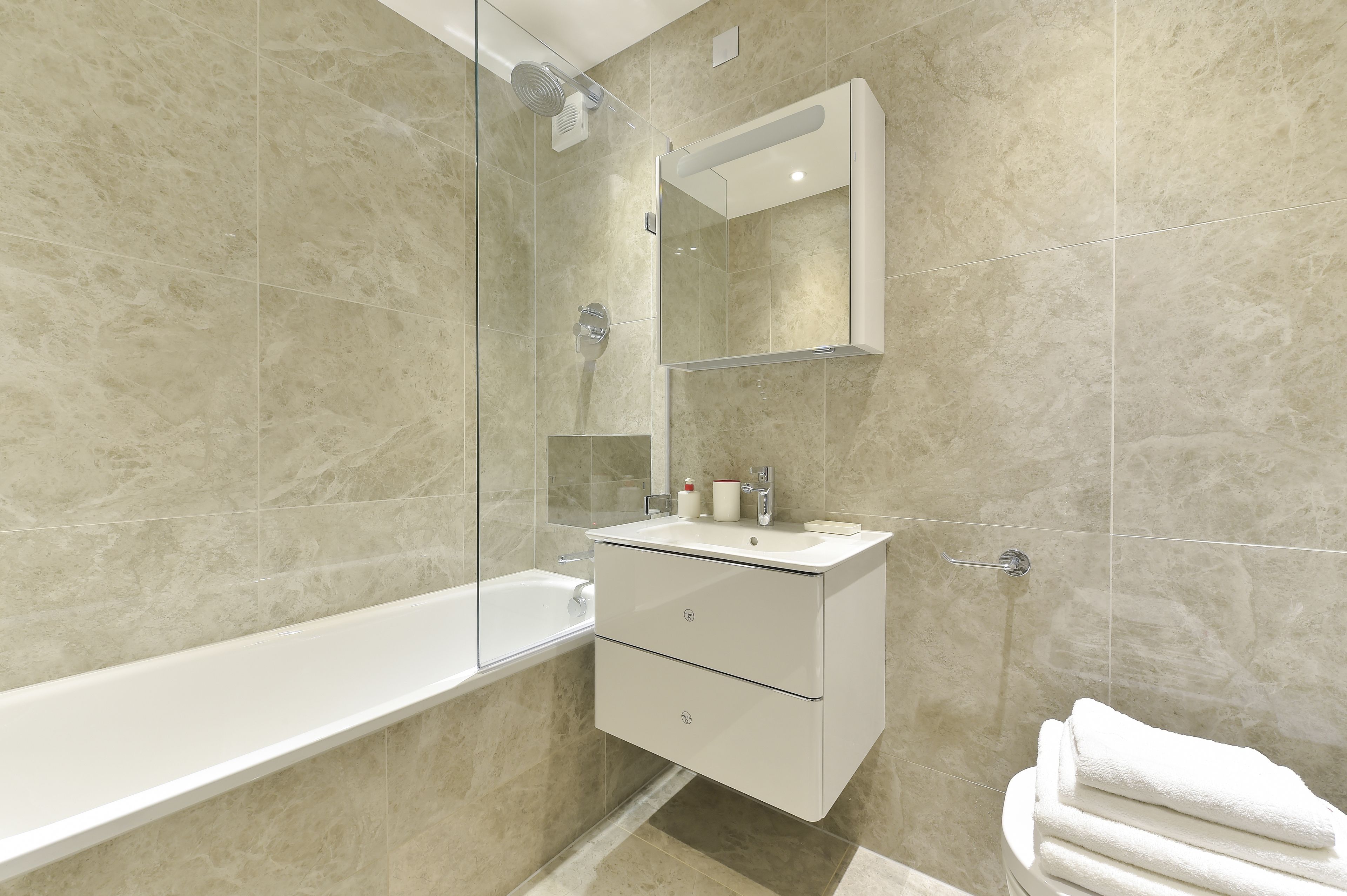 A modern bathroom with a glass-enclosed shower, a white vanity with a mirror, and a white bathtub.