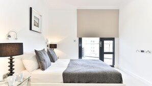 Ein modernes Schlafzimmer mit einem Bett, Nachttischlampen, einem Glastisch mit Tassen, einem Fenster mit Blick und einem großen Fensterladen.