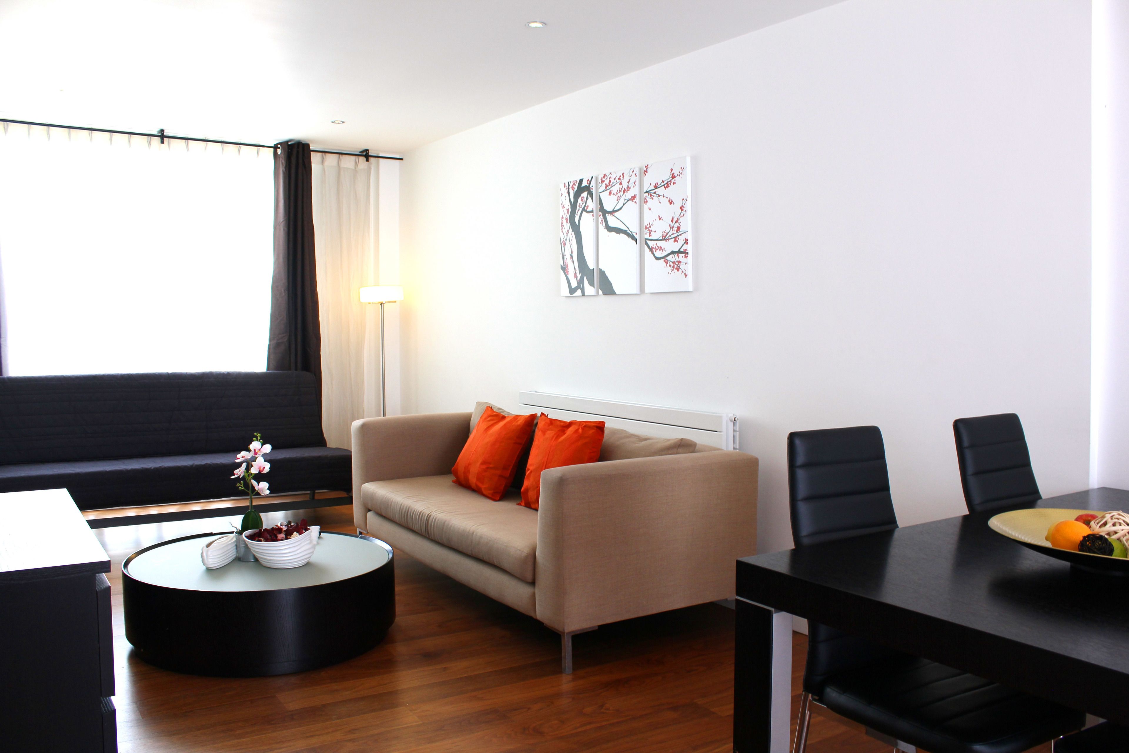 Uma sala de estar moderna com um sofá, uma mesa de centro redonda e uma mesa de jantar com cadeiras.