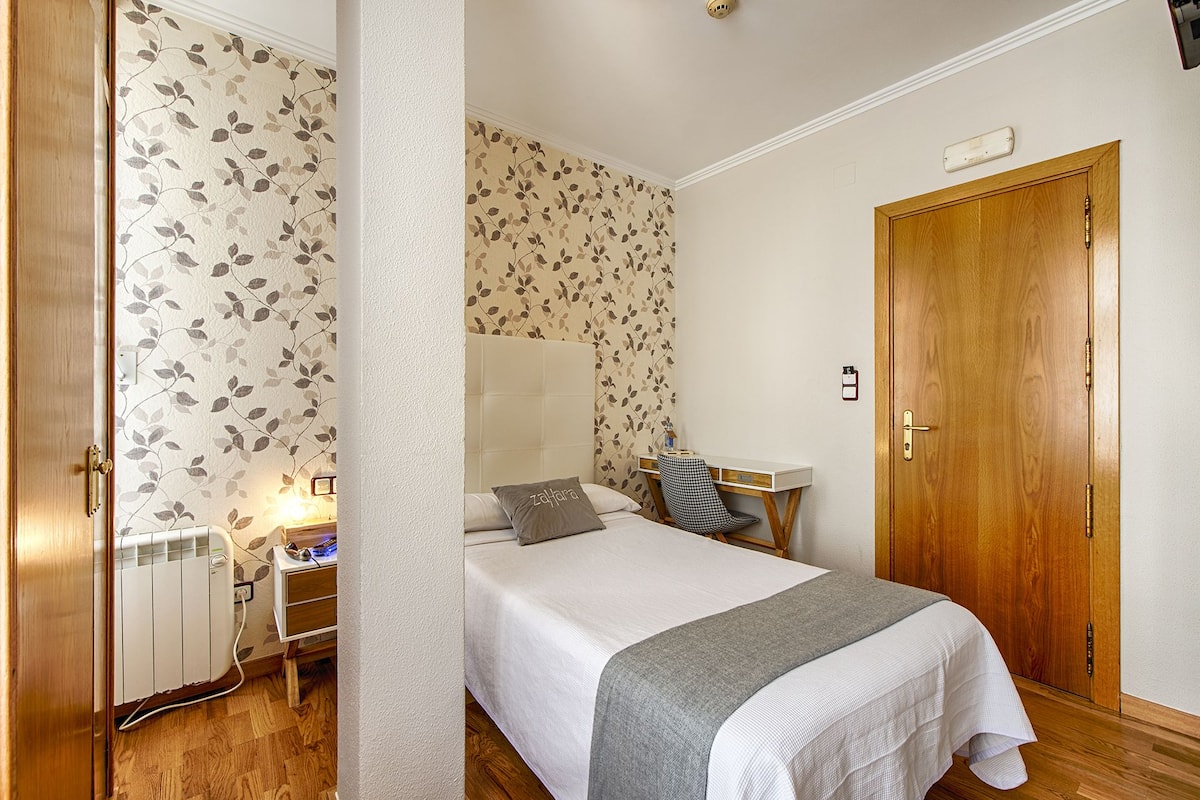 Un dormitorio con cama, mesita de noche, lámpara y puerta de madera.