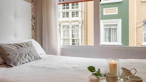 A hotel room with a bed, a window with curtains, and a view of buildings outside. - Hostal Zahara (Ferrol)