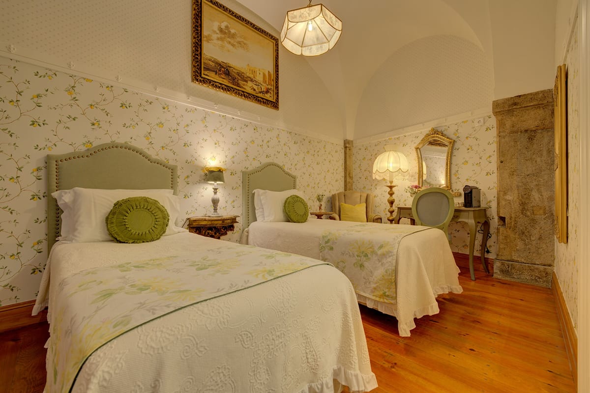 Een kamer met twee bedden, bloemenbehang, een kroonluchter en een spiegel.