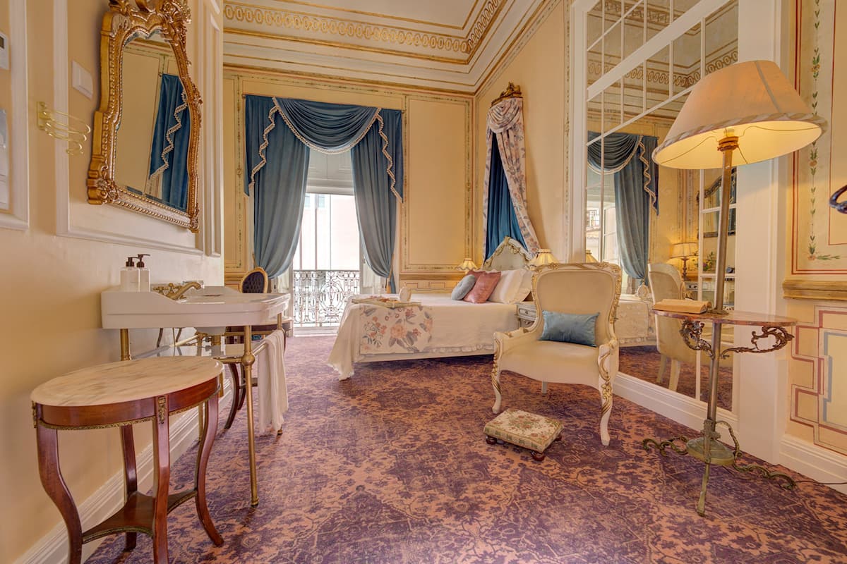 Een luxueuze slaapkamer met een groot bed, sierlijk meubilair en een klassieke kroonluchter.