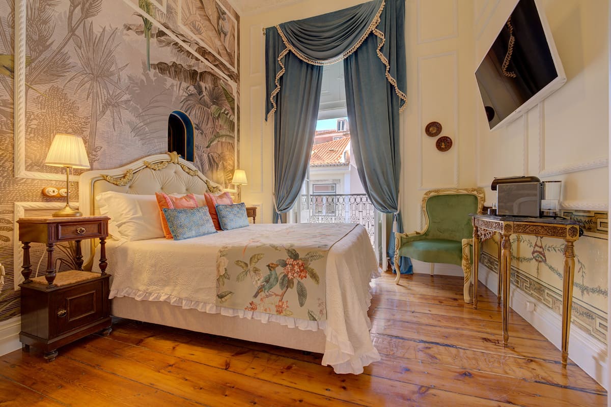 Een slaapkamer met een bed, een nachtkastje, een groene fauteuil, een kleine tafel en een aan de muur bevestigde televisie.