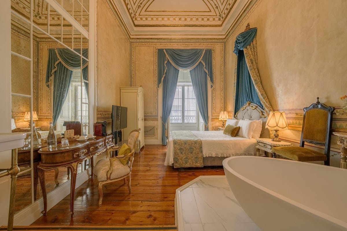 Een klassieke hotelkamer met een houten vloer, een groot bed met een witte hemel, een zithoek met een stoel en een klein tafeltje, en een ruime badkuip.