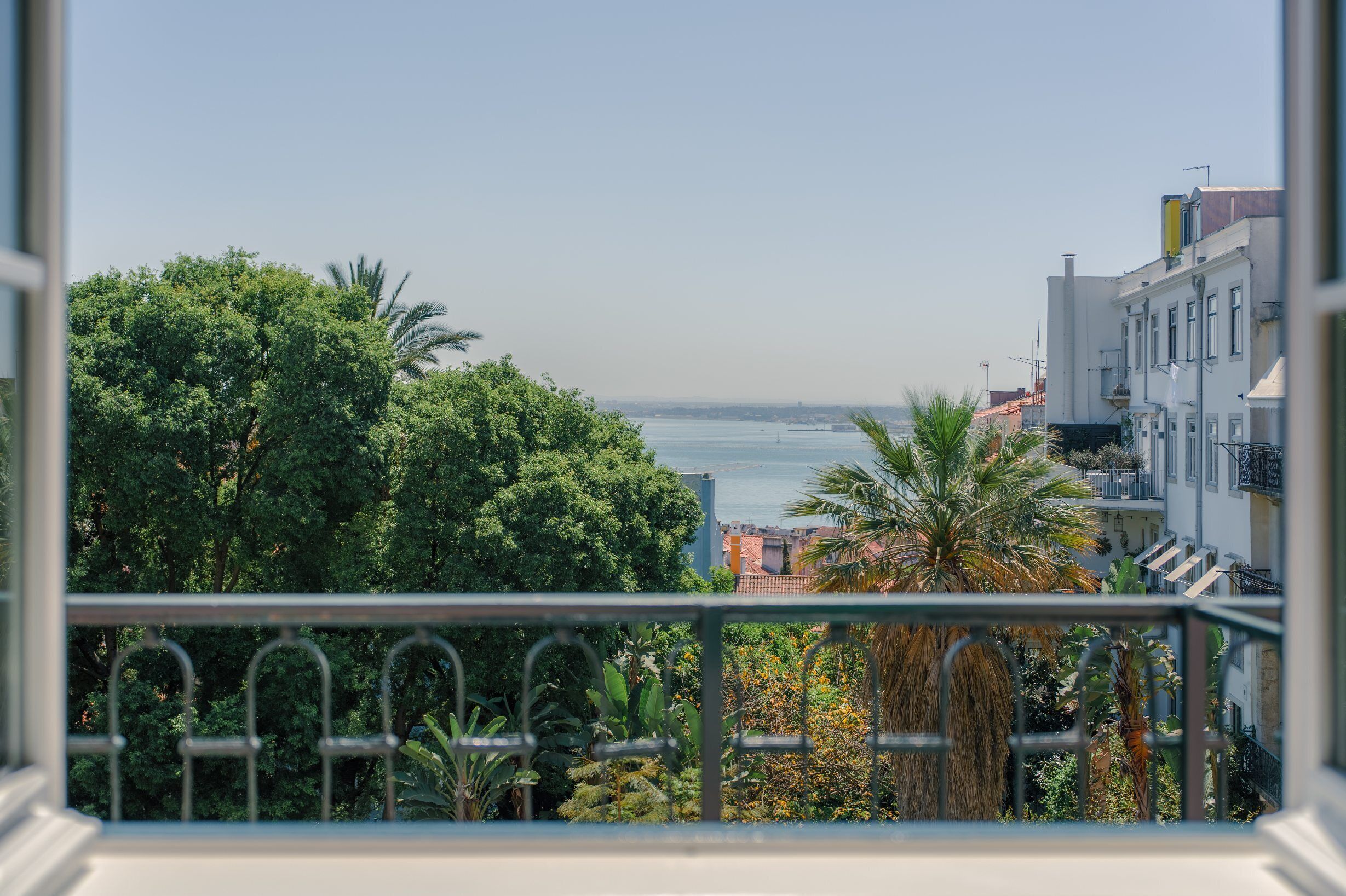 Een balkon met uitzicht op de zee, weelderige begroeiing en gebouwen op de achtergrond.