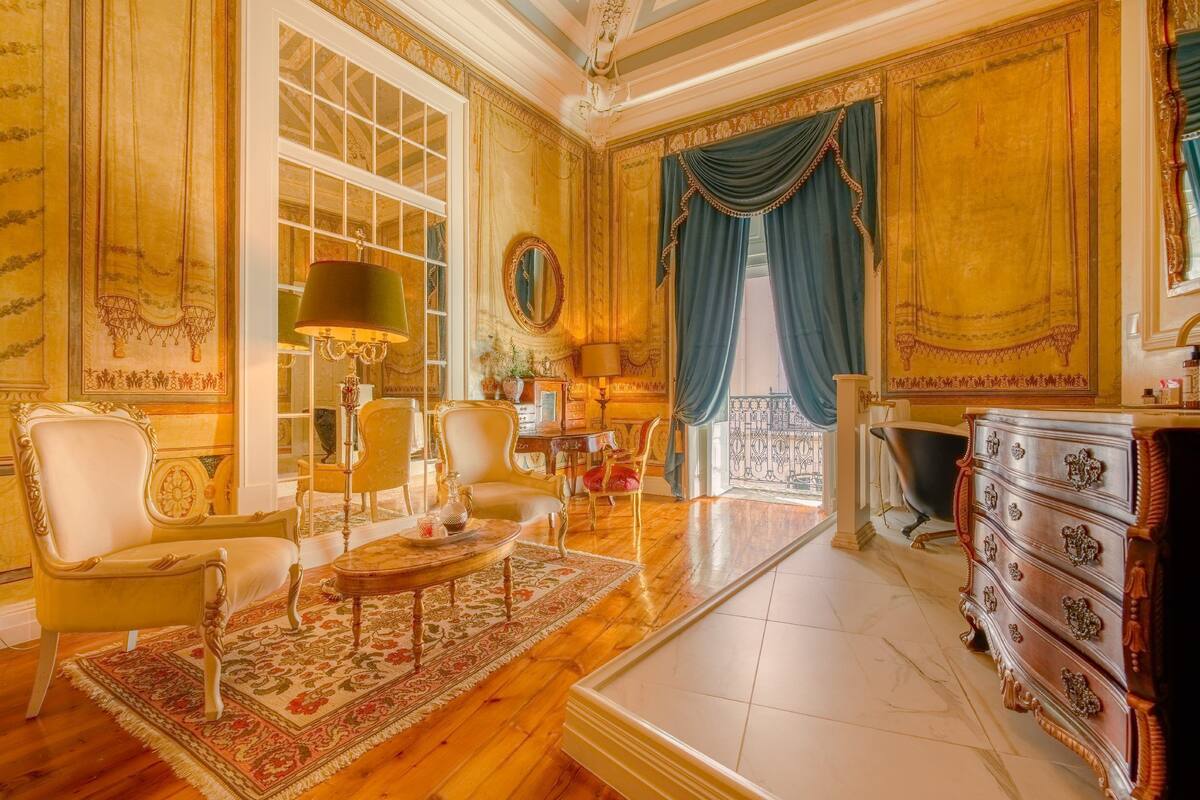 Een luxueuze kamer met een groot raam, versierde meubels en een klassieke kroonluchter.