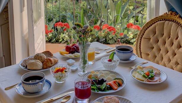 A dining table set with various dishes and drinks, overlooking a garden with flowers and trees. - Palácio das Especiarias (Lisbon)