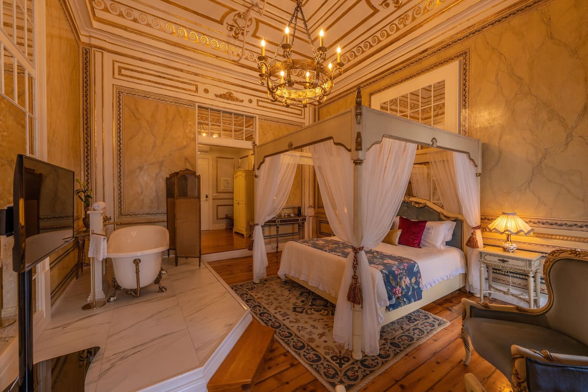 Een luxueuze slaapkamer met een hemelbed, een badkuip en een kroonluchter.