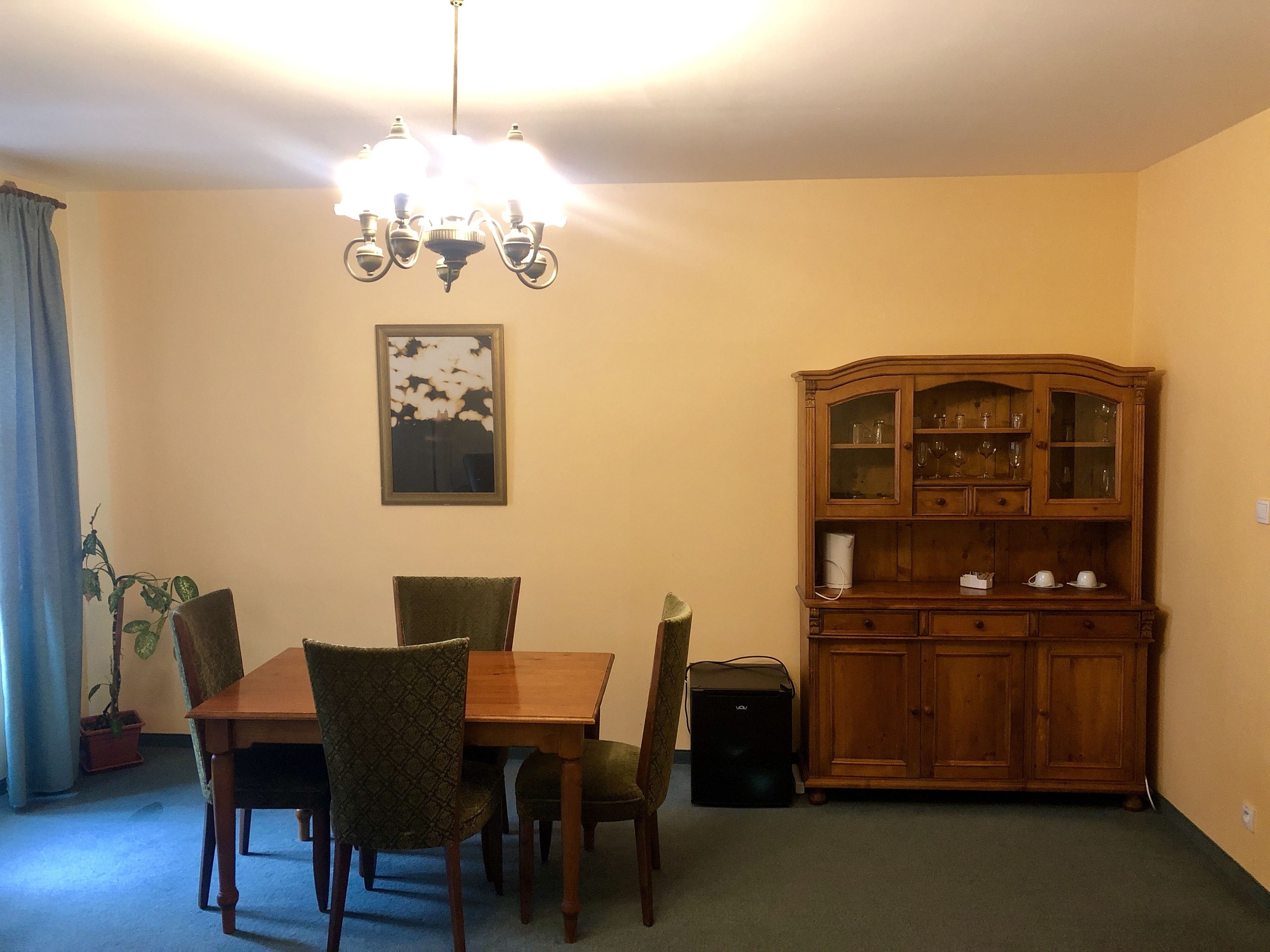 A dining area with a wooden table, four chairs, a chandelier, a cabinet with glass doors, and a framed picture on the wall.