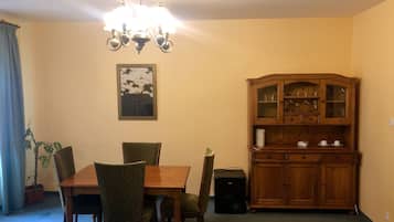 A dining area with a wooden table, four chairs, a chandelier, a cabinet with glass doors, and a framed picture on the wall.