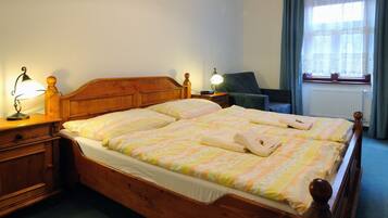 A double bed with a wooden headboard, two bedside tables with lamps, a chair, and a window with curtains.