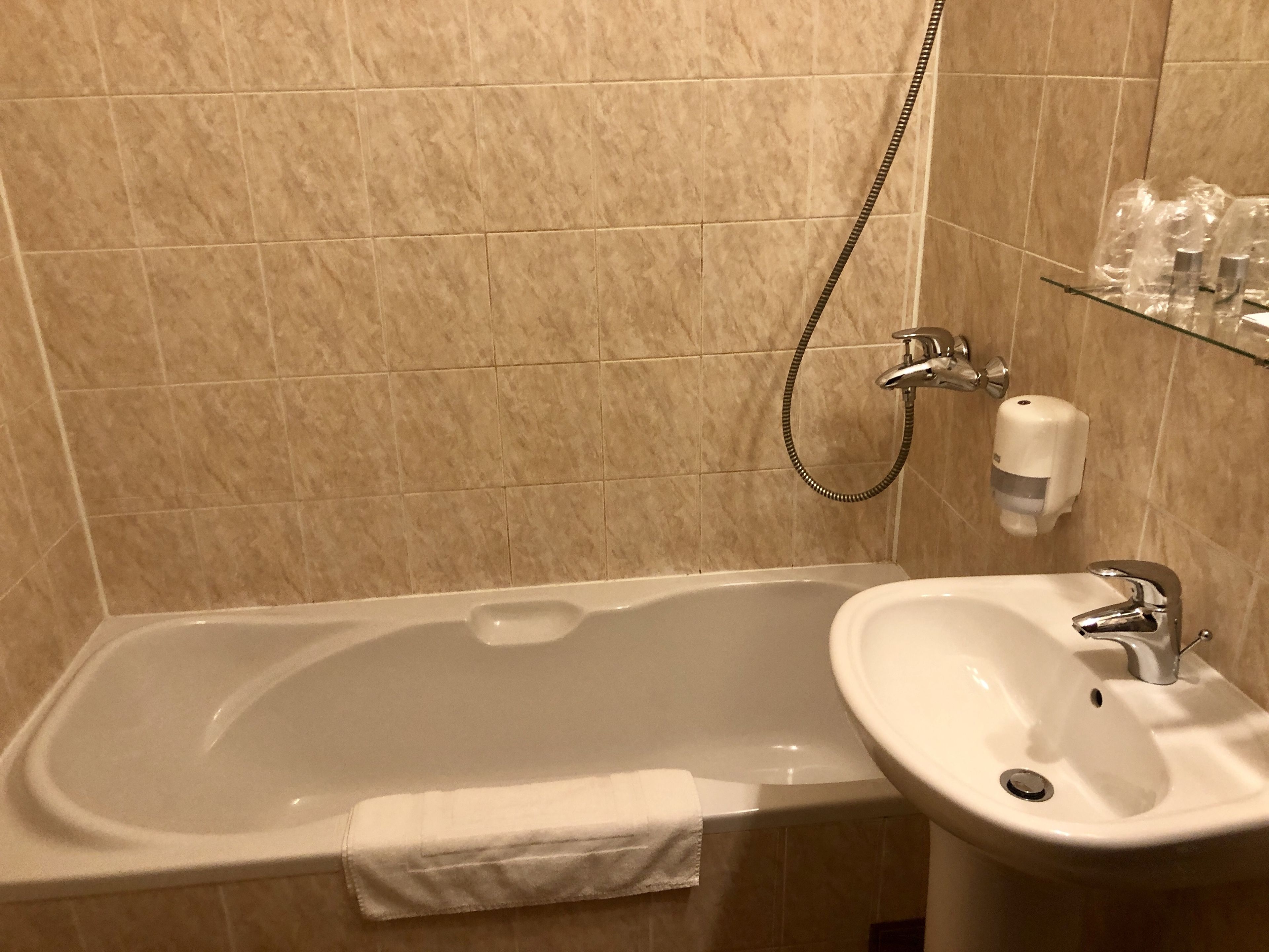 Un baño con bañera, lavamanos y estante de vidrio con artículos de aseo.