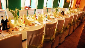 Ein Festsaal mit langen Tischen, gedeckt für eine festliche Veranstaltung, mit weißen Tischdecken, ordentlich gedeckten Plätzen und floralen Tischdekorationen.