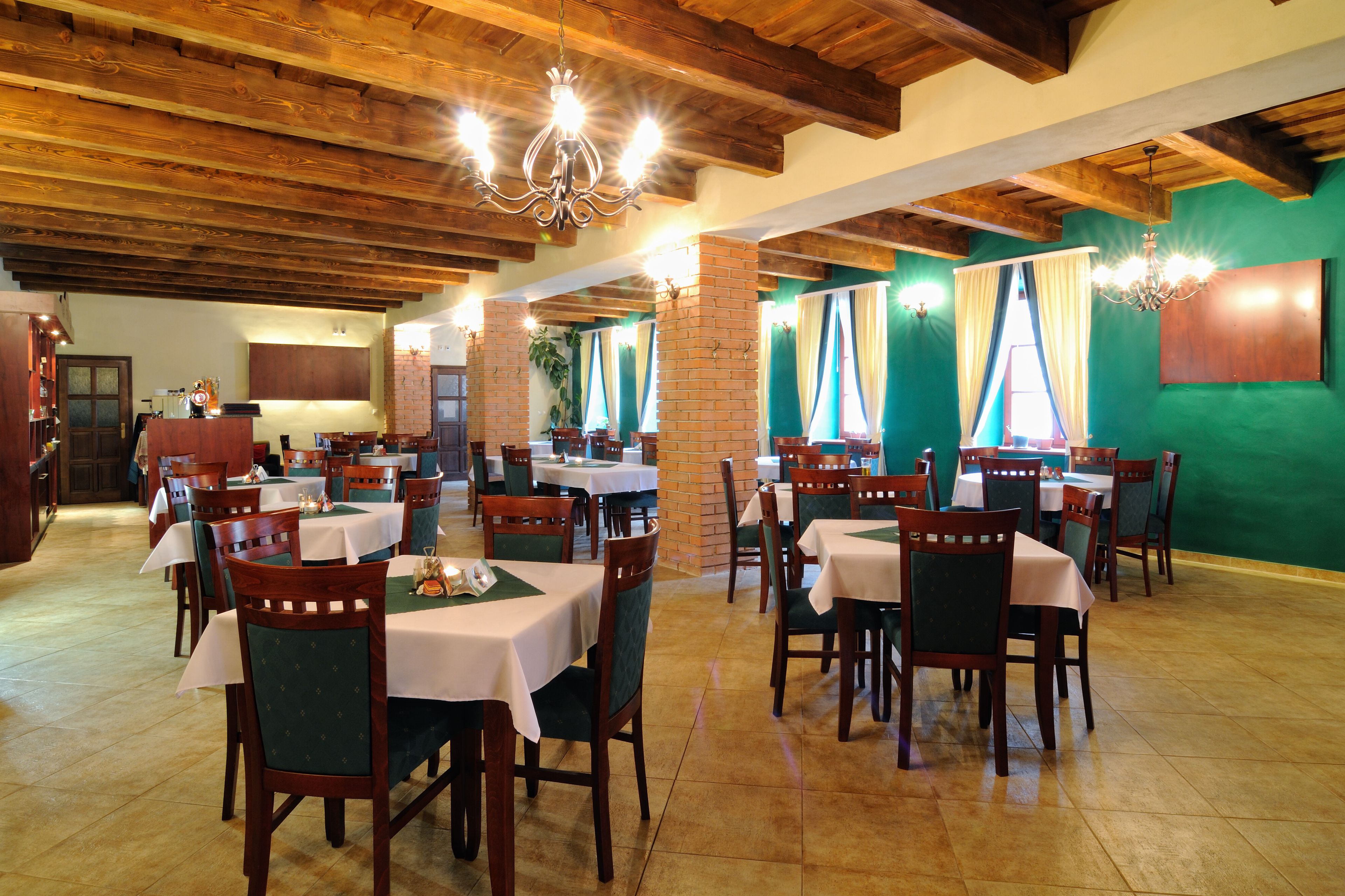 Ein Restaurant mit Holzbalken, grünen Wänden und mehreren Tischen mit Stühlen.