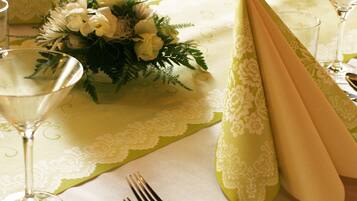 Una mesa dispuesta para una cena elegante, con cubertería fina, servilletas decorativas y un centro de mesa con flores.