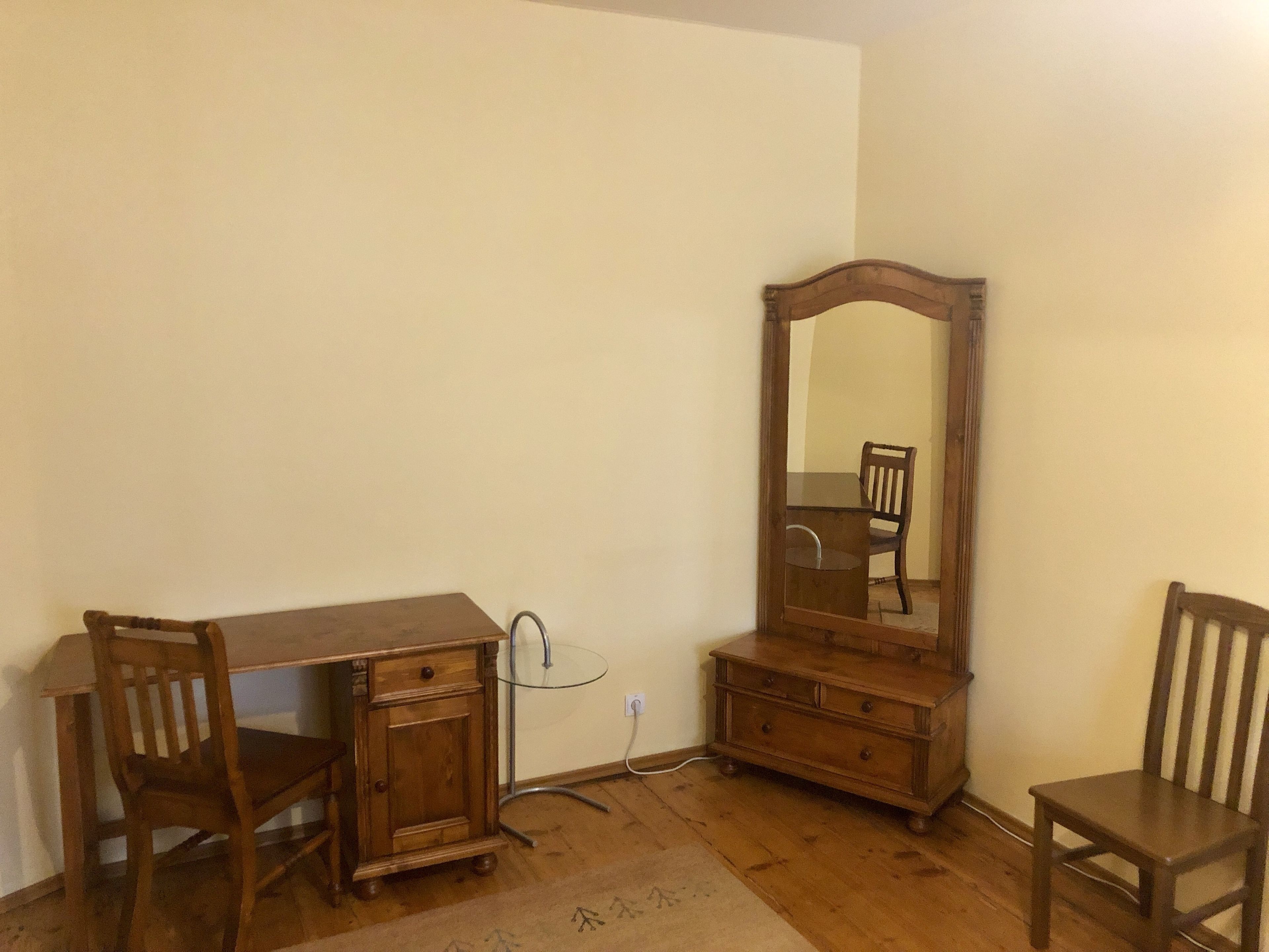 A room with a wooden desk, a chair, a dresser, and a mirror.