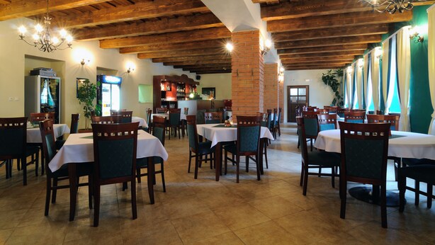 Ein Restaurant mit Holzbalken, Tischen mit weißen Tischdecken und grünen Stühlen.