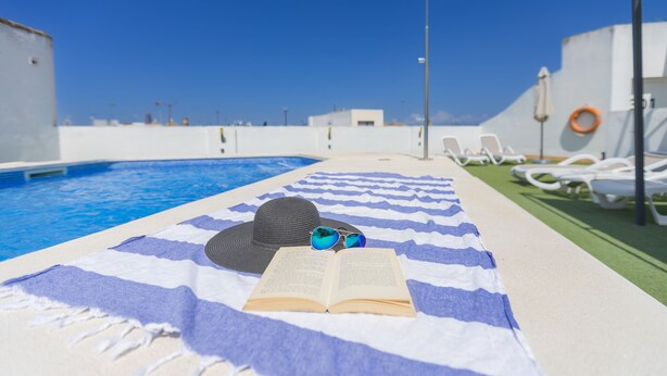 A poolside area with a blue and white striped towel, a hat, sunglasses, and an open book. - Hotel ITC Artemisa by Soho Boutique (Seville)