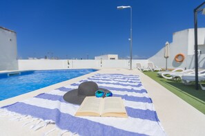 A poolside area with a blue and white striped towel, a hat, sunglasses, and an open book. - Hotel ITC Artemisa by Soho Boutique (Seville)
