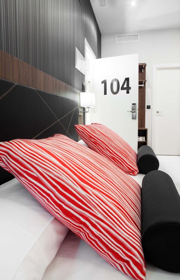 A modern hotel room with a large bed, red and white striped pillows, a black headboard, and a white door with the number 104. - Hotel ITC Artemisa by Soho Boutique (Seville)