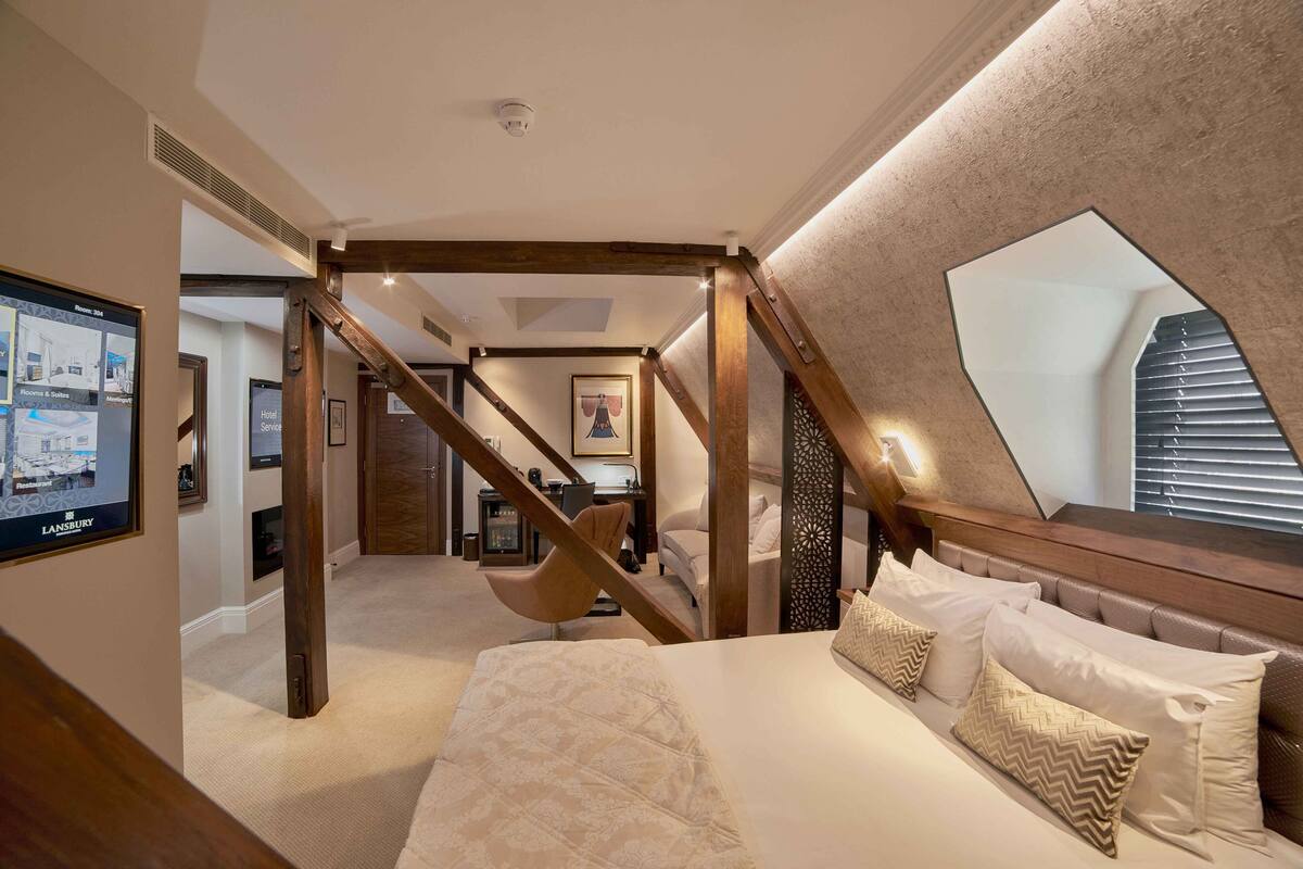 A bedroom with a large bed, a wooden staircase, a desk, and a large mirror.