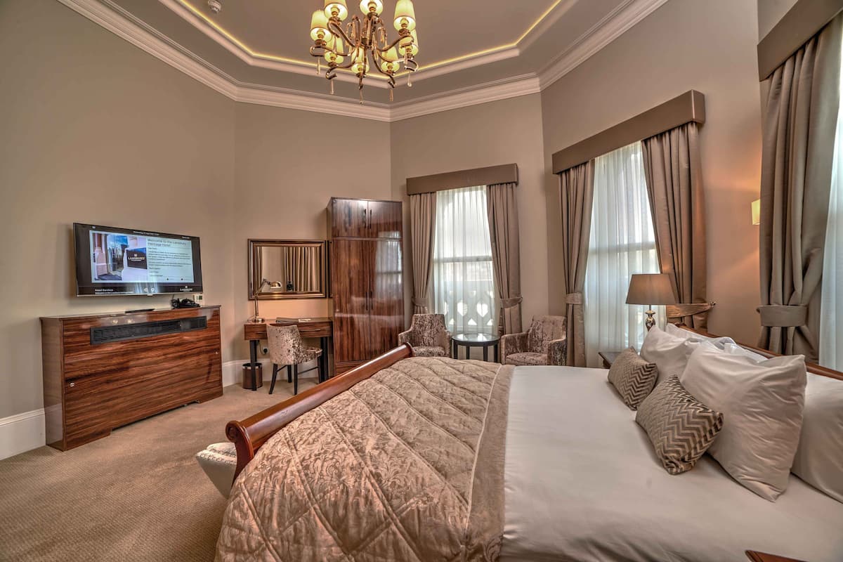 A hotel room with a large bed, a desk with a computer, a television, and a chandelier.