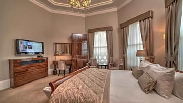 A hotel room with a large bed, a desk with a computer, a television, and a chandelier.