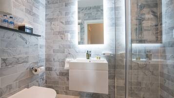 Une salle de bain moderne avec des carreaux de marbre, une douche en verre, un lavabo blanc avec un miroir et des toilettes.