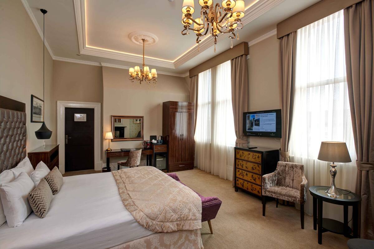 A hotel room with a large bed, a desk with a computer, a television, and a chandelier.