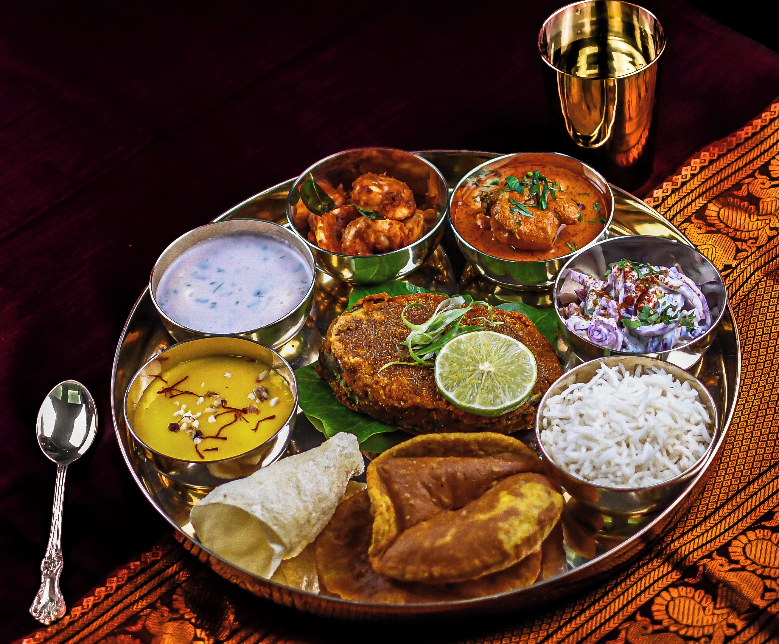 A traditional Indian meal served on a metal tray with various dishes including curry, rice, and a samosa.