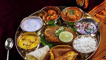 A traditional Indian meal served on a metal tray with various dishes including curry, rice, and a samosa.