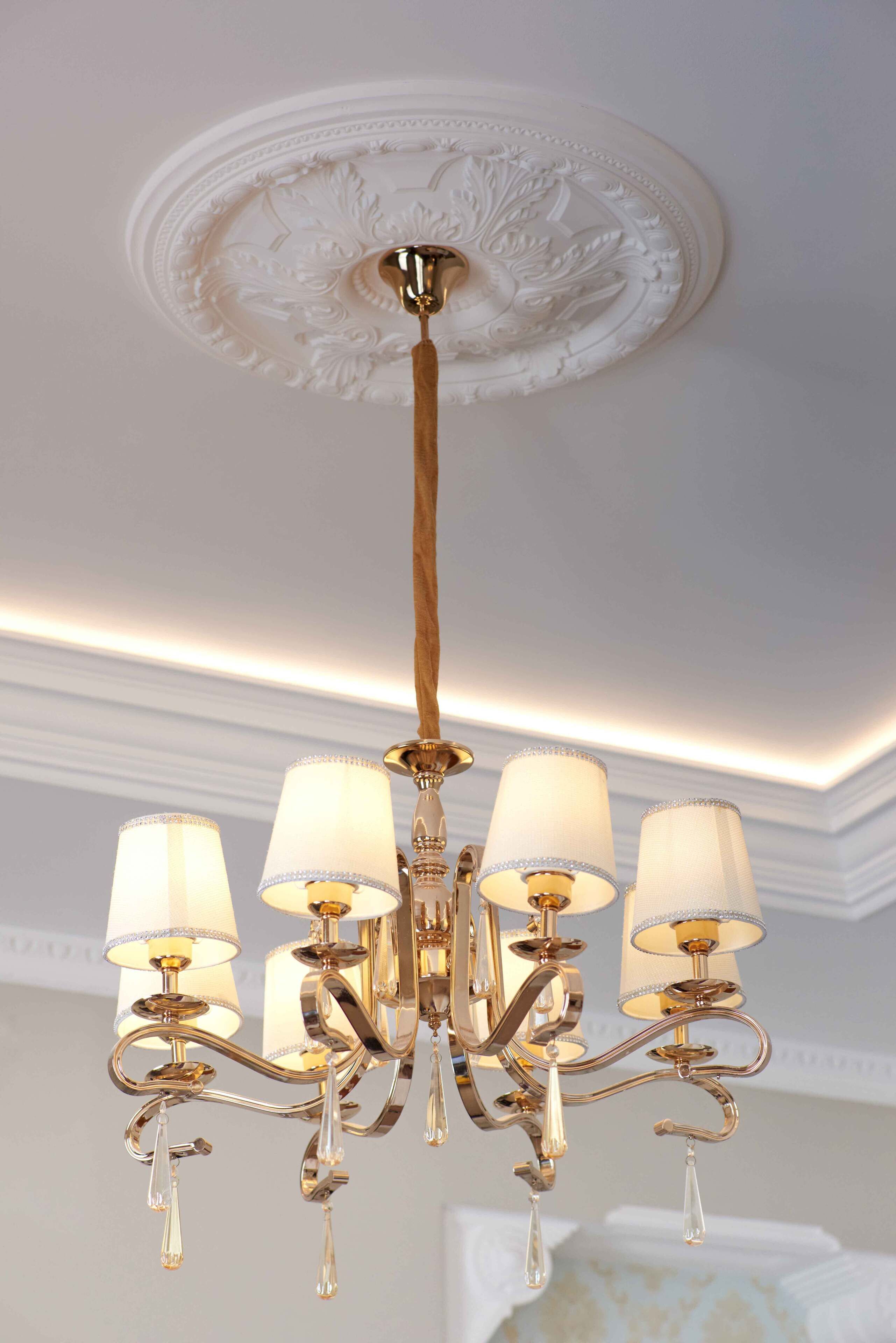 A chandelier with multiple arms and lampshades, hanging from an ornate ceiling.