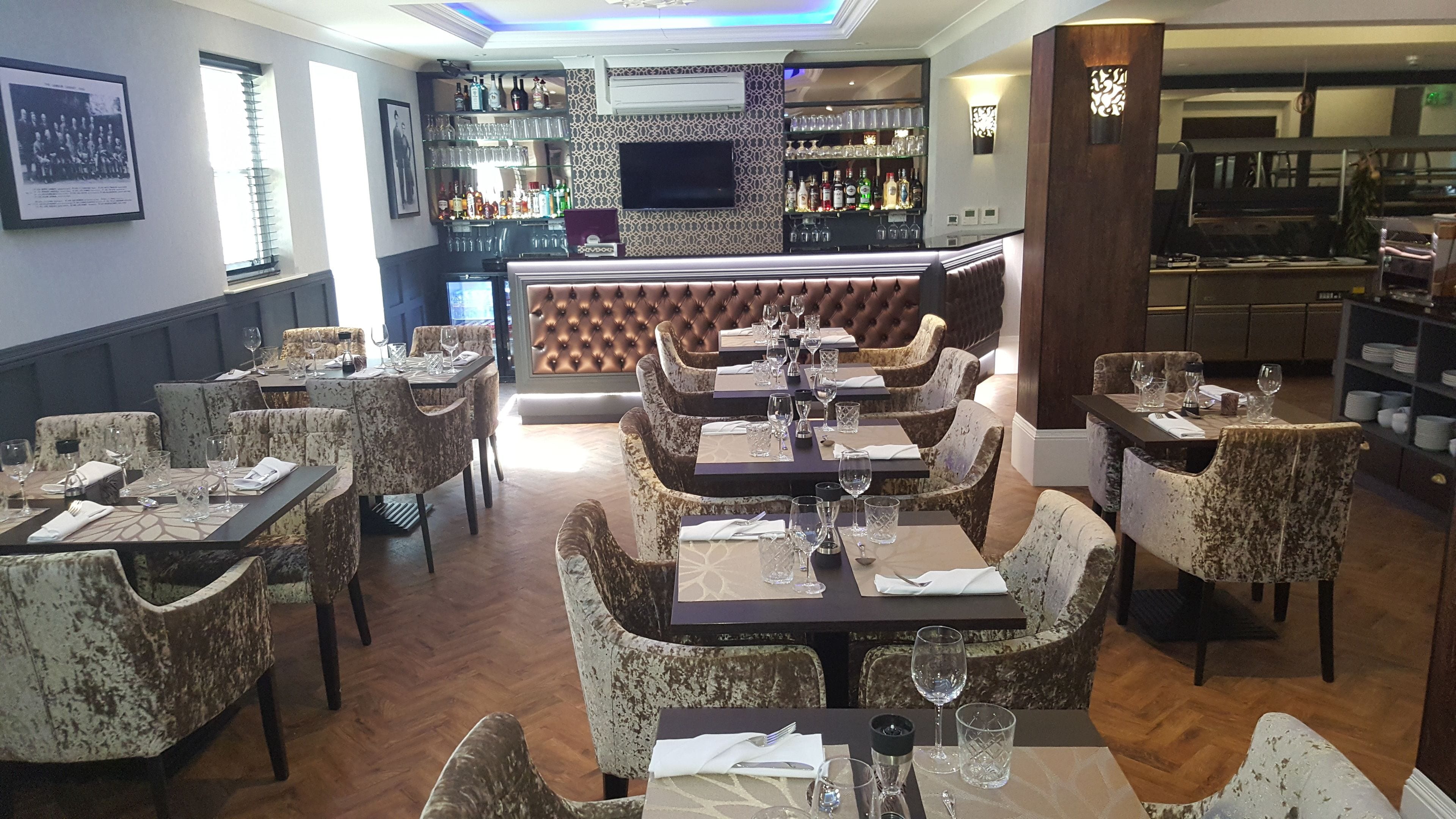 A restaurant with a bar area, multiple dining tables with chairs, and a variety of bottles and glasses on shelves.