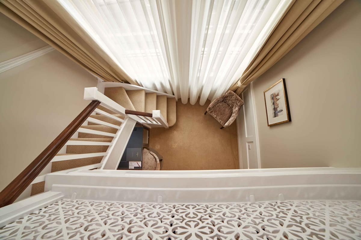 A staircase with a wooden handrail, beige carpet, and a patterned white floor.