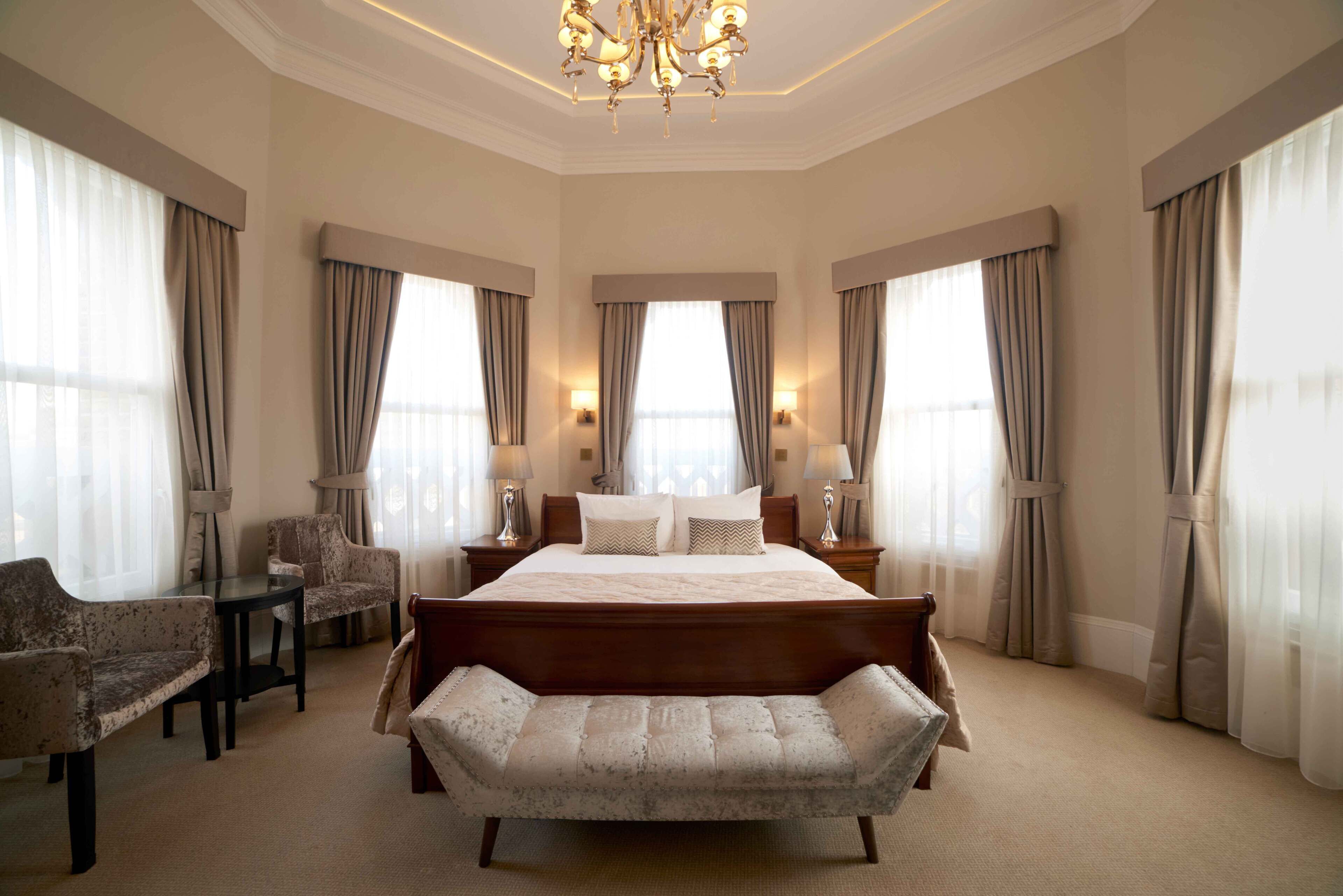 Ein geräumiges Schlafzimmer mit einem großen Bett, einer Bank, zwei Sesseln, einem kleinen Tisch und einer Chandelüster.