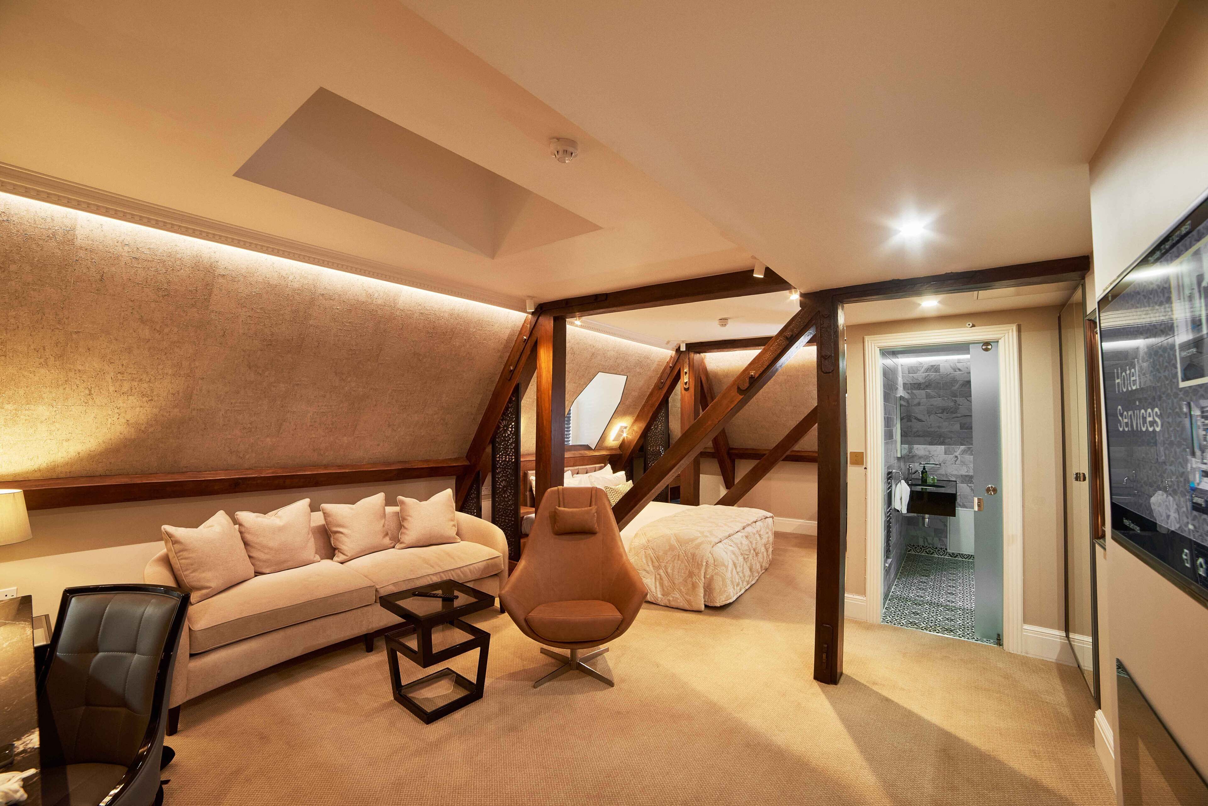 A modern loft bedroom with a sloped ceiling, a sofa, a chair, and a bed.
