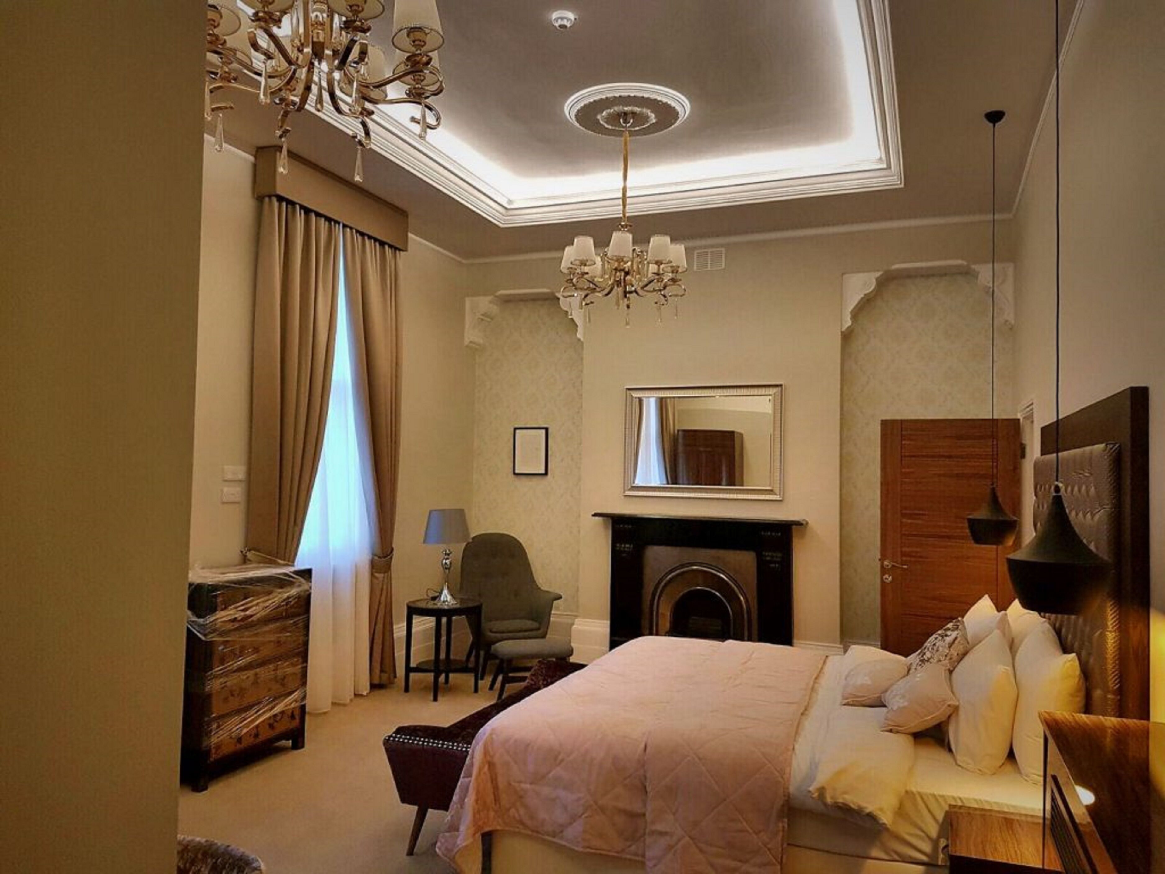 A hotel room with a bed, a fireplace, a chandelier, and a mirror.
