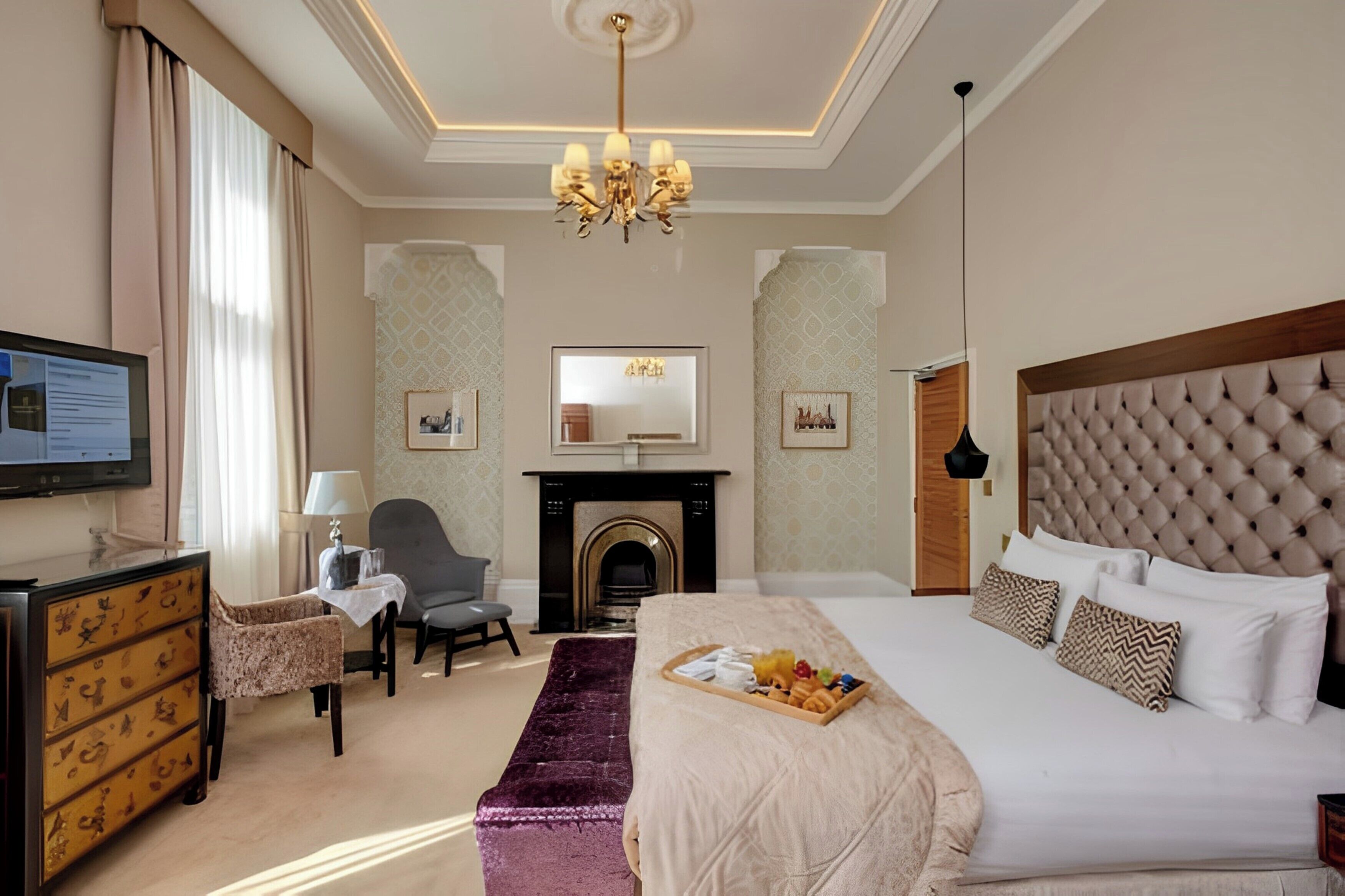 Una habitación de hotel con una cama grande, televisión, chimenea y escritorio con lámpara.