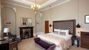 Une chambre d’hôtel élégamment aménagée, dotée d’un grand lit, d’une cheminée, d’un coin salon avec un banc et d’un bureau avec une lampe.