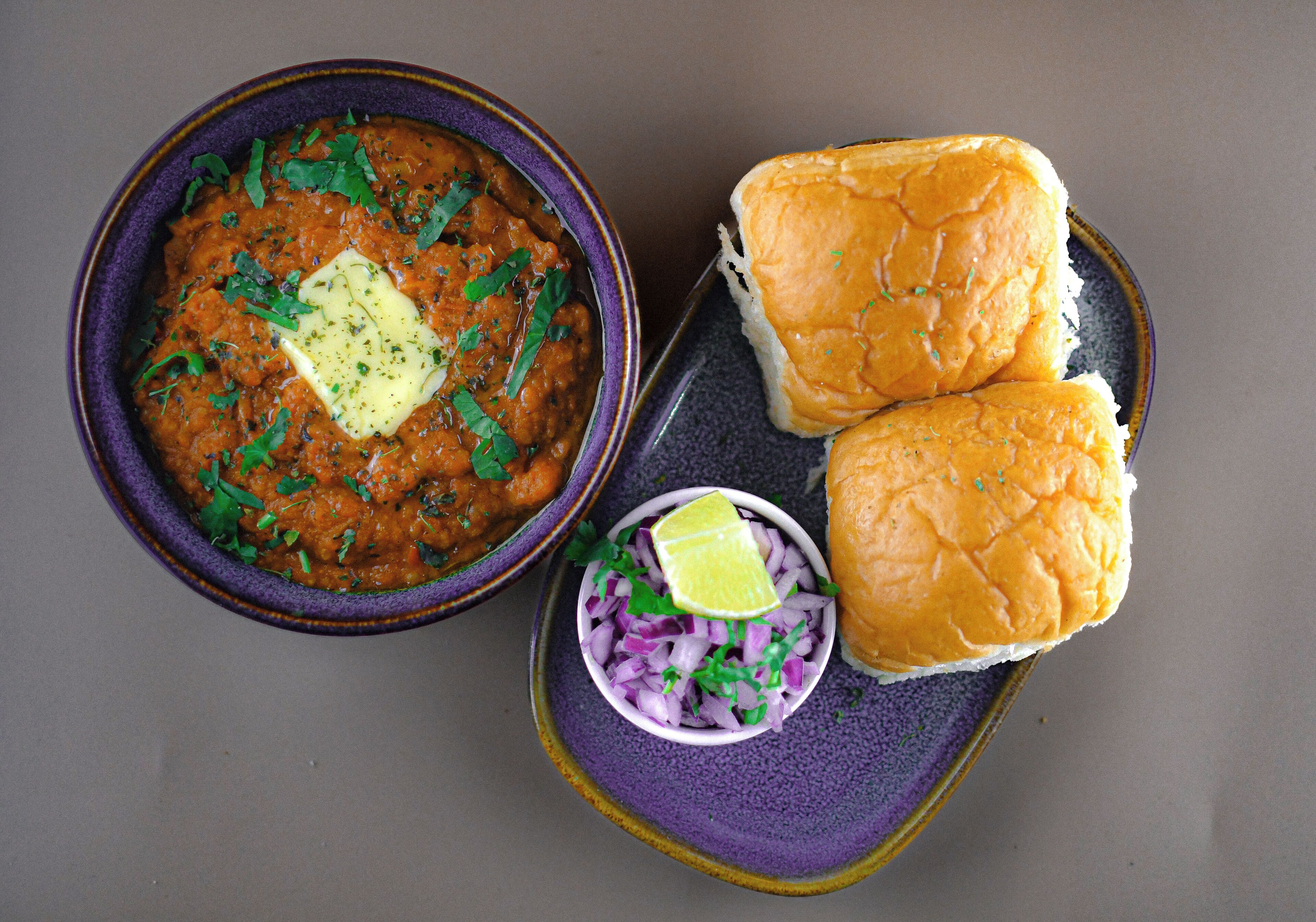 Eine Schüssel Curry mit Butterflocken und gehackten Zwiebeln, dazu zwei Brötchen und eine kleine Schale mit Zwiebeln.